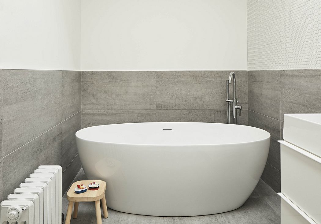 Modern bathroom with a large, oval-shaped bathtub, gray tiles, and a wooden stool.