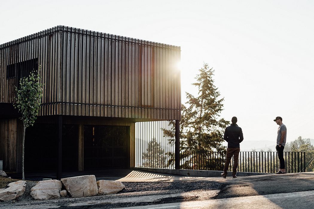Striking modern exterior with vertical metal panels, stone, and sunlit trees.