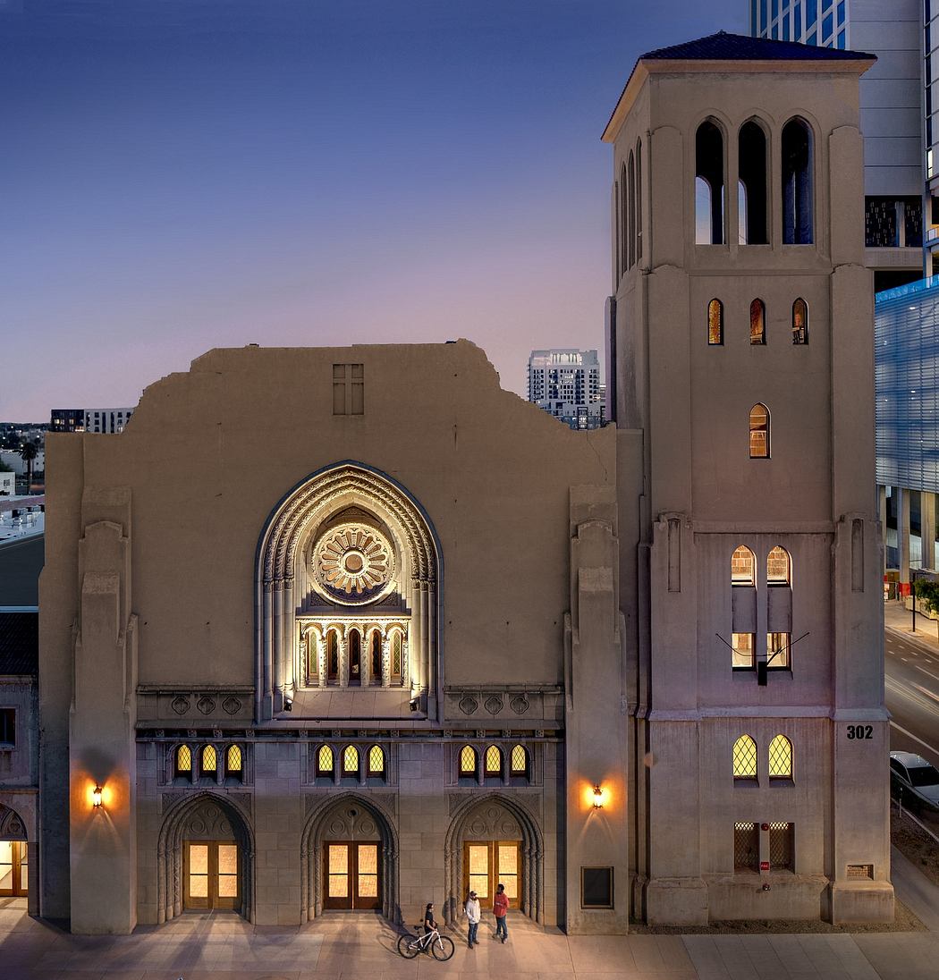 Ornate architectural facade with arched windows, decorative stone carvings, and illuminated interiors.