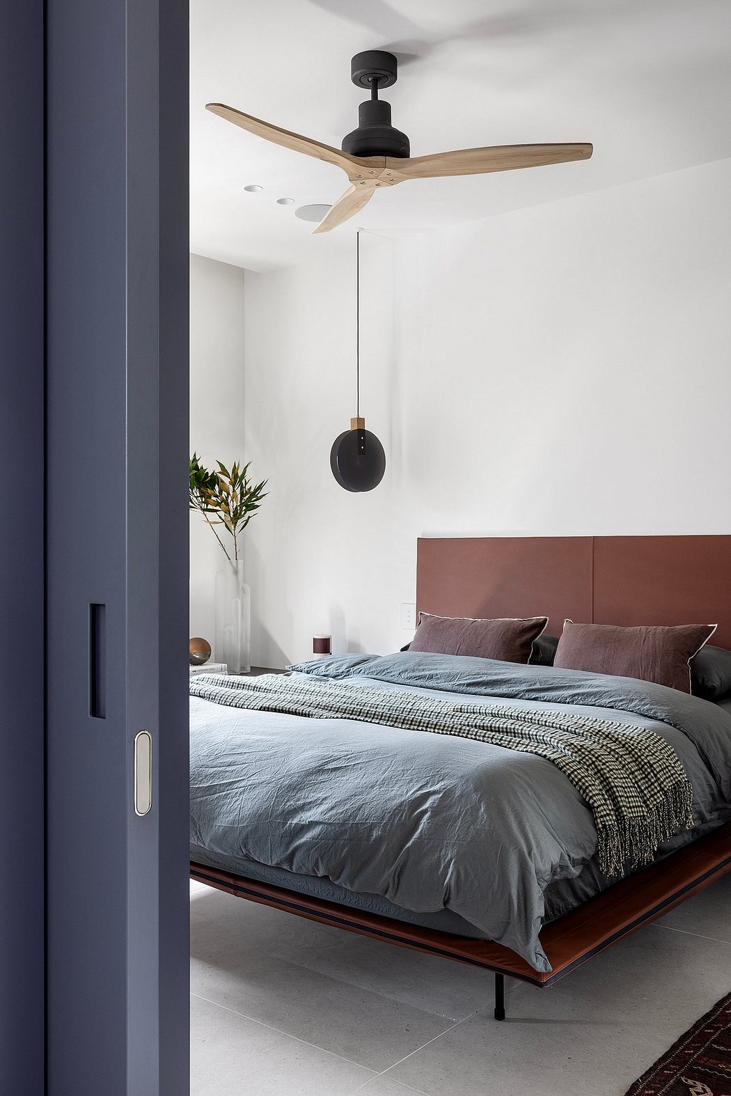 Minimalist bedroom with wooden ceiling fan, dark bedframe, and plant decor.