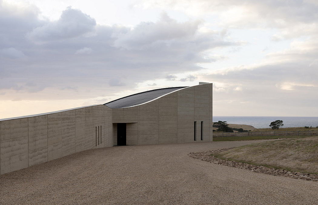 A modern, concrete building with a curved roofline overlooking a coastal landscape.