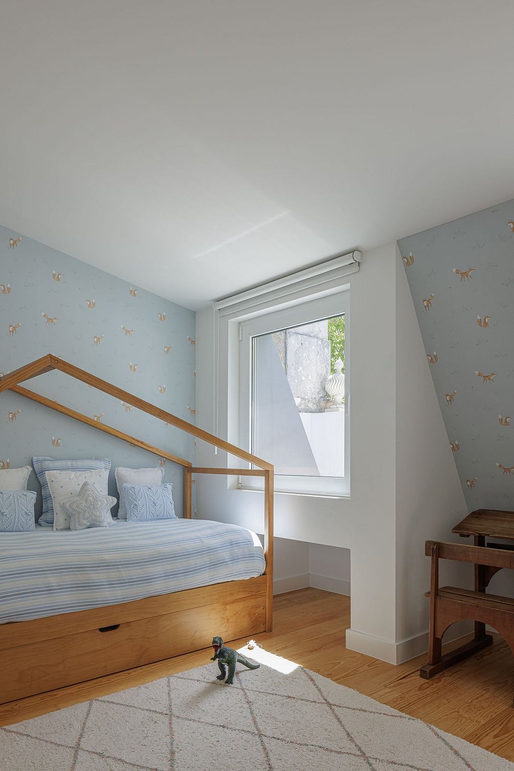 Cozy bedroom with wood frame bed, patterned wallpaper, and large window letting in natural light.