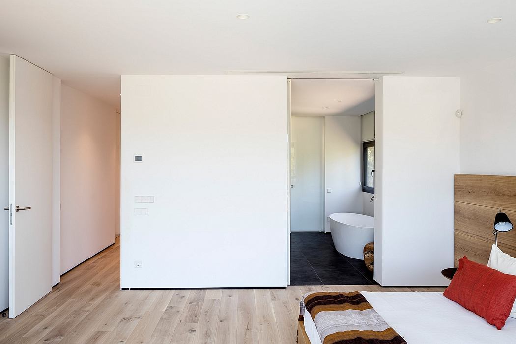 Minimalist bedroom with wooden floors, white walls, and ensuite bathroom visible.