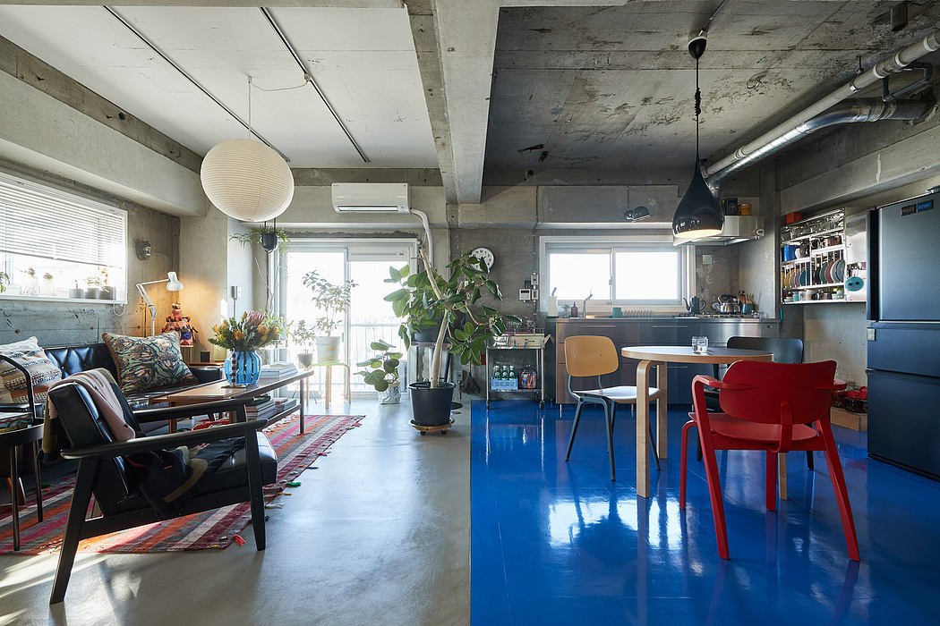 Eclectic industrial-style living space with concrete walls, vibrant blue floor, and varied furnishings.