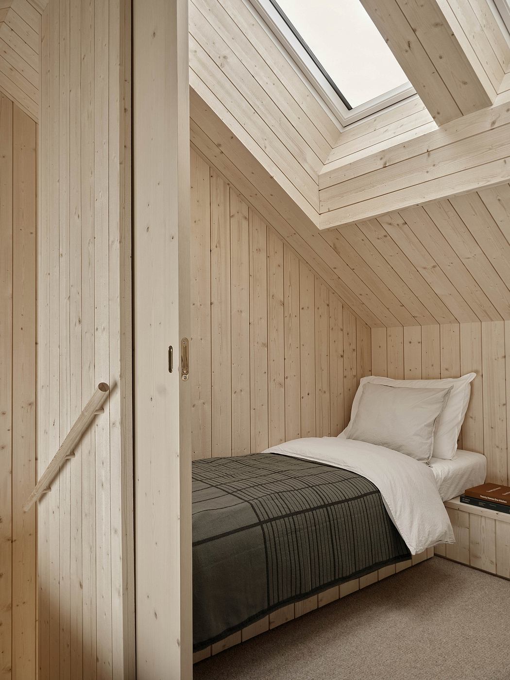A cozy attic bedroom with wooden walls, slanted ceiling, and large skylight.