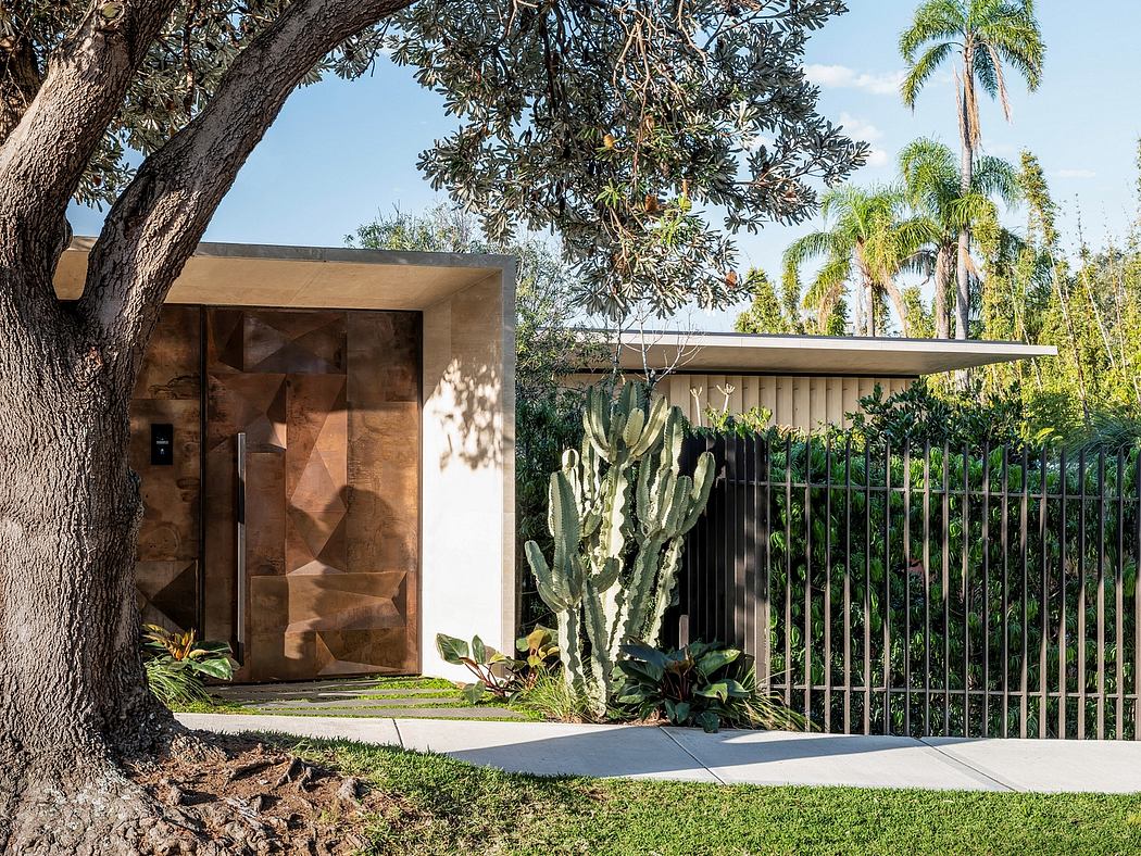 A modern, minimalist house with a distinctive stone facade and a lush, tropical landscape.