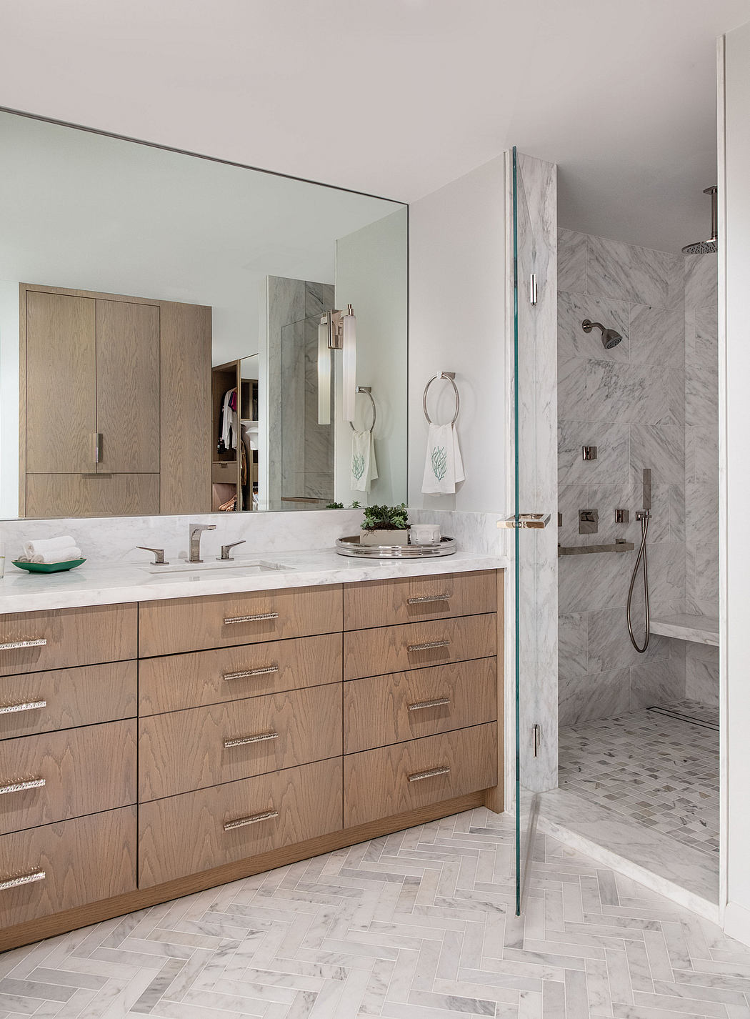 Sleek modern bathroom with marble tiles, glass shower, and wooden vanity drawers.