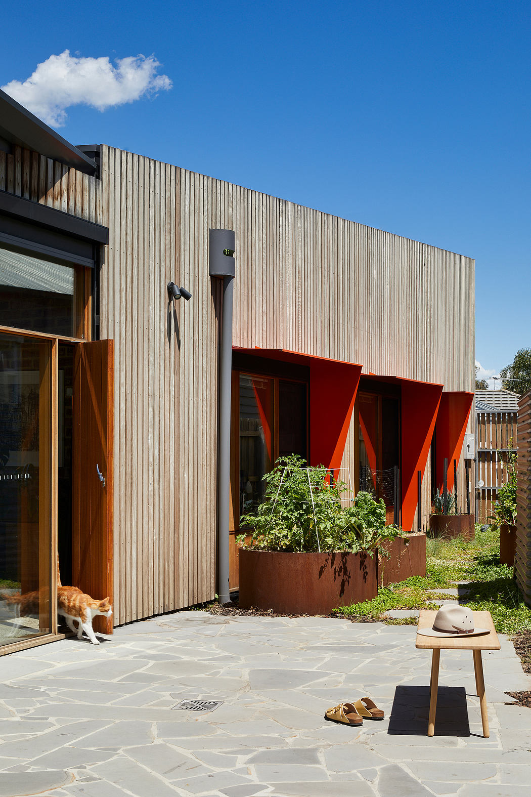 Distinctive wooden facade, red-framed entry, embedded garden planter, natural stone paving.