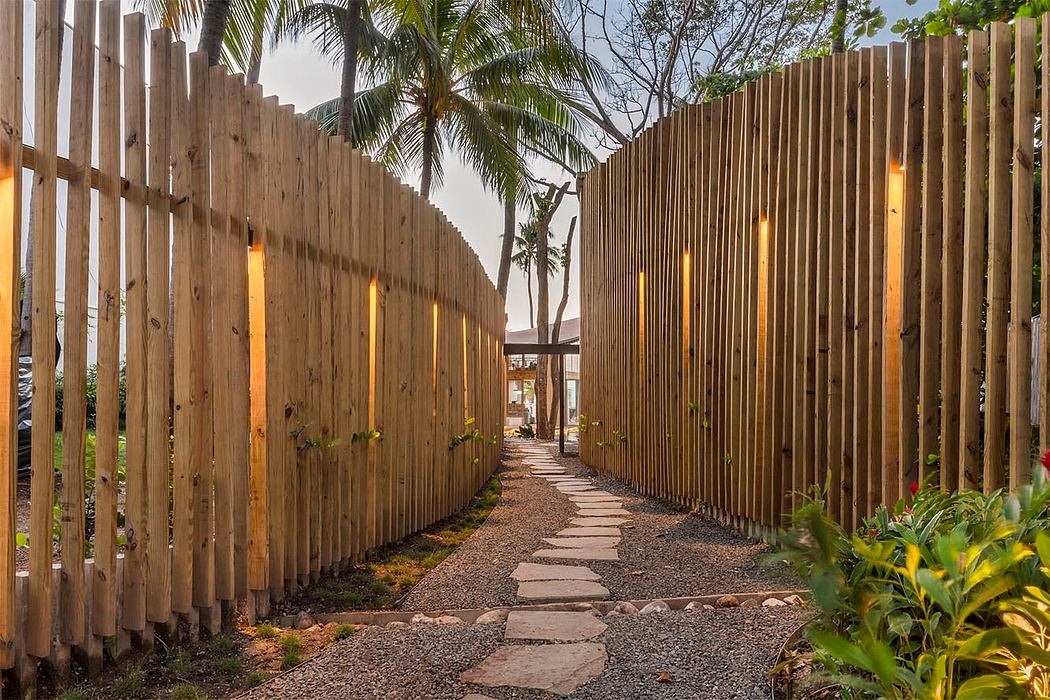 A rustic wooden fence frames a winding pathway lined with lush tropical foliage.