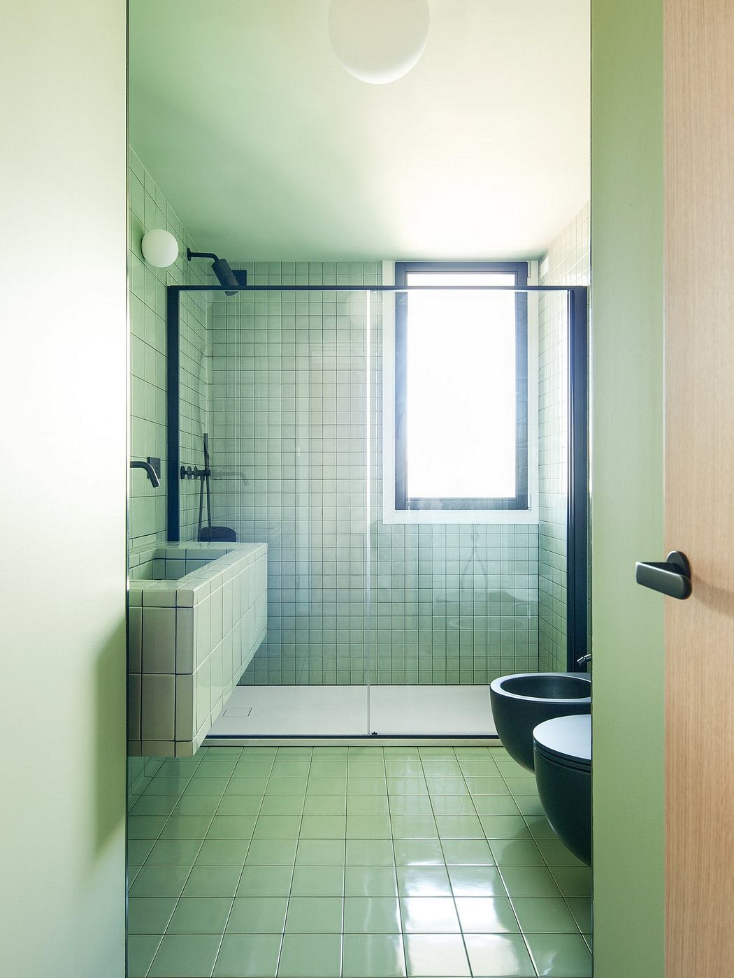 Minimalist bathroom interior with green tile walls, window, and modern black fixtures.