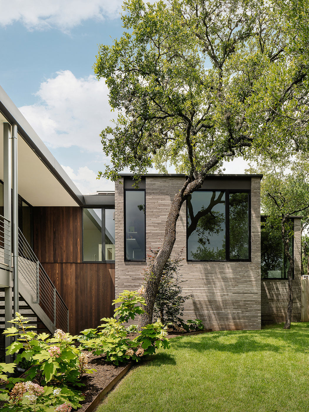 Modern home with brick exterior, large windows, and mature tree canopy providing shade.