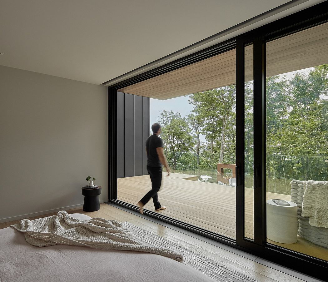 Modern bedroom with large sliding glass doors overlooking a lush outdoor deck and forest.