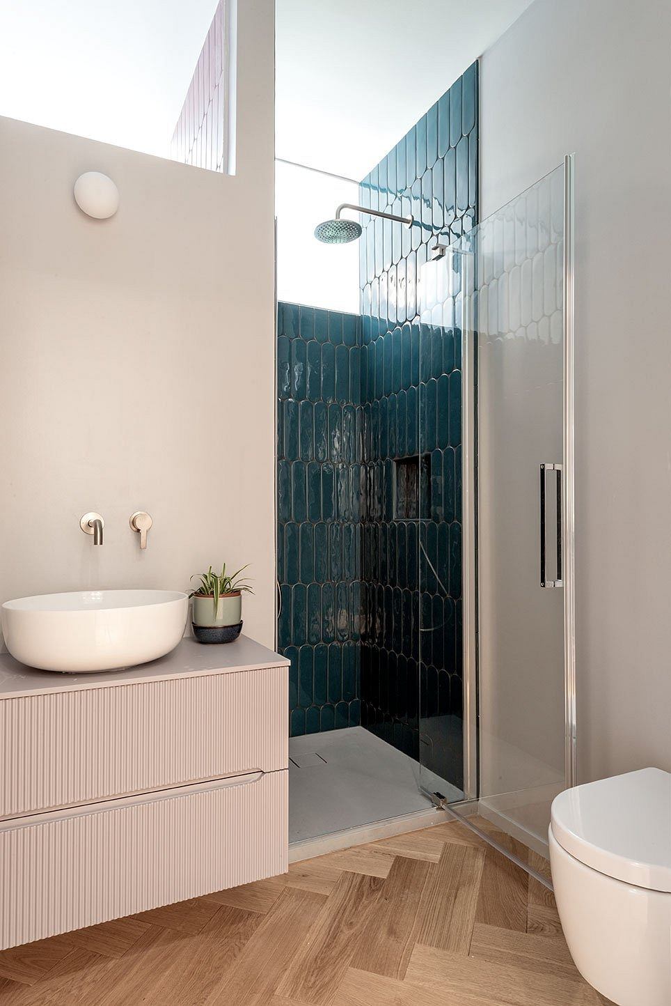 Sleek, minimalist bathroom with herringbone wood floors, teal tile shower, and modern vanity.