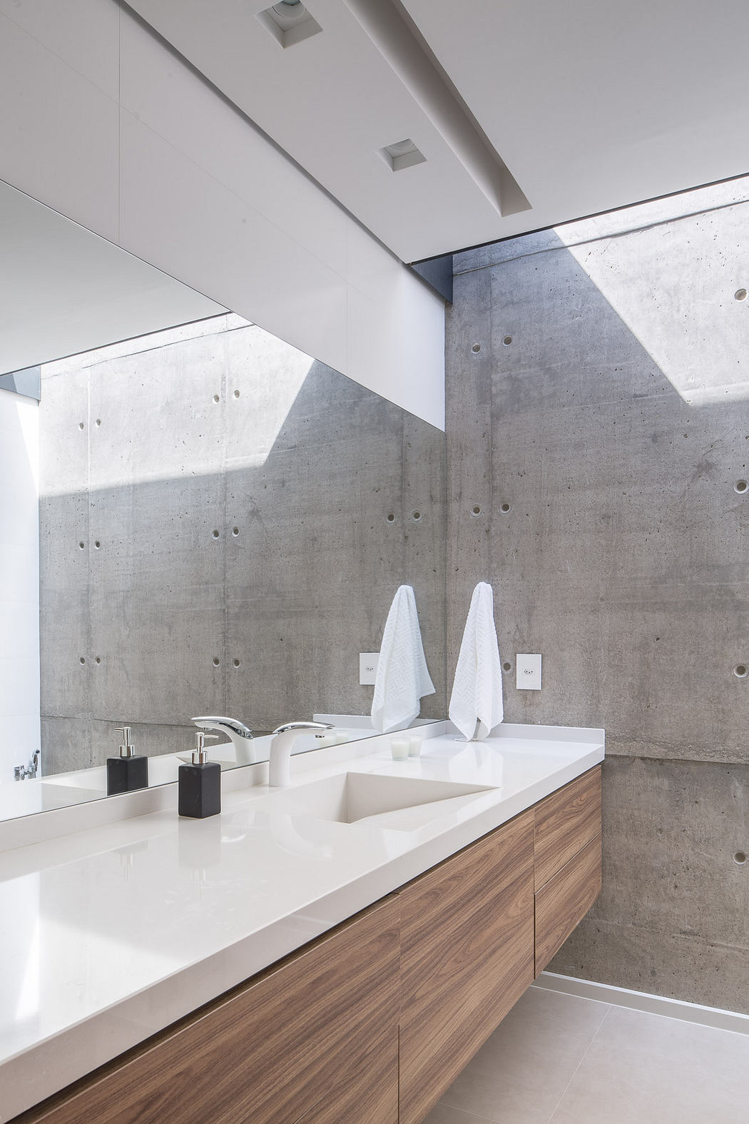 Sleek, modern bathroom with concrete walls, white countertop, and wood cabinetry.