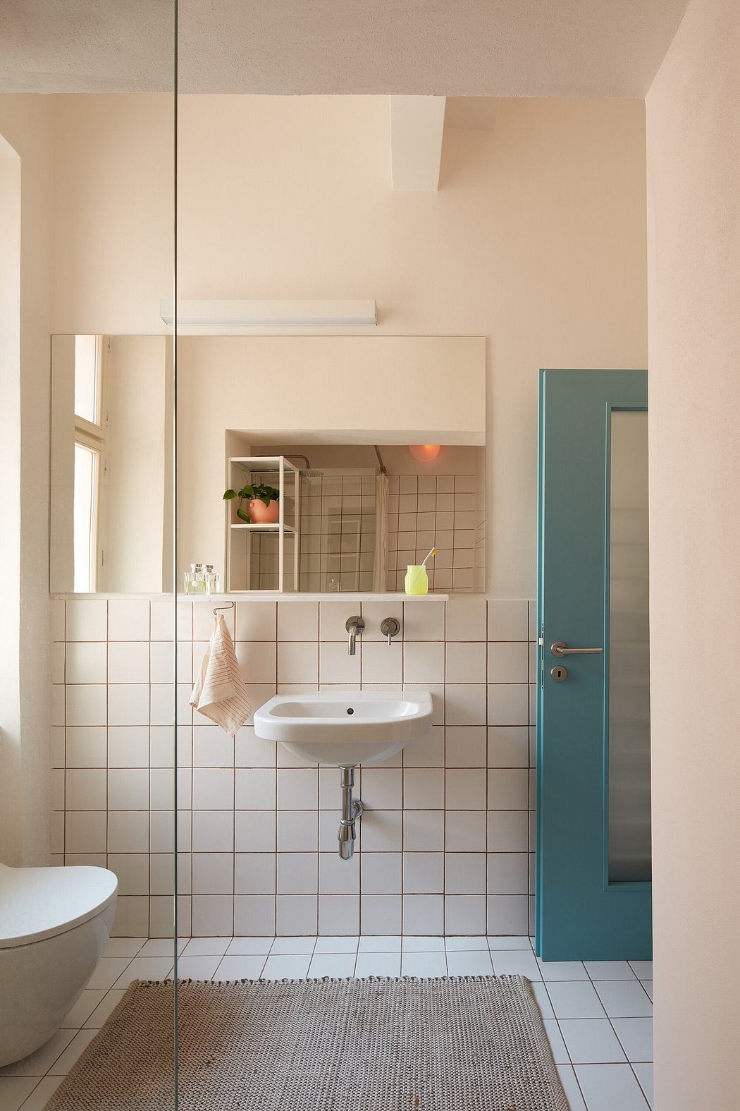 A warm, minimalist bathroom with tiled walls, a pedestal sink, and a vibrant blue door.