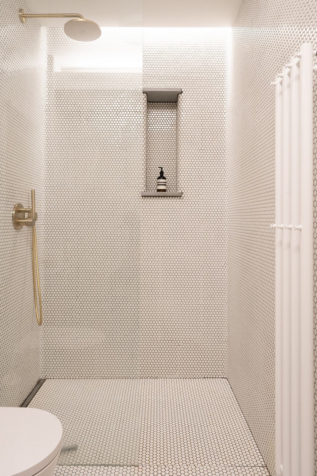 Sleek, modern bathroom with hexagonal tile pattern, minimalist shelving, and overhead shower.