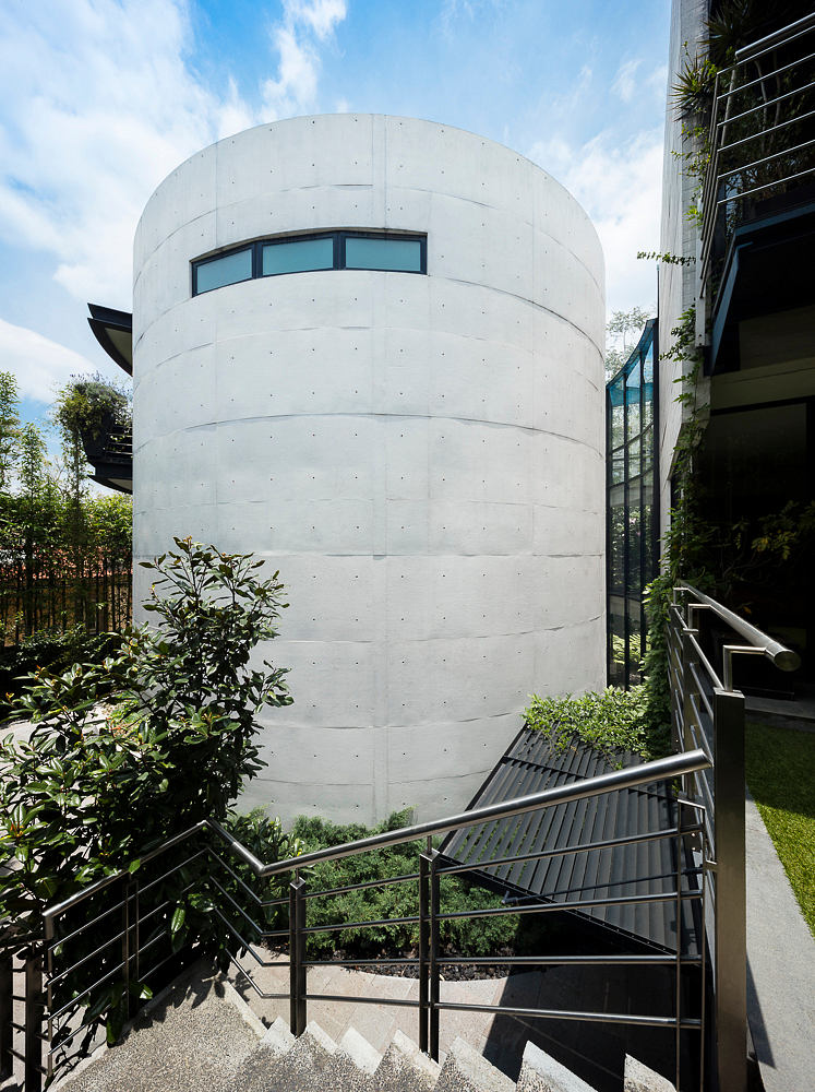 A striking circular concrete structure with encircling stairs and large windows, surrounded by greenery.