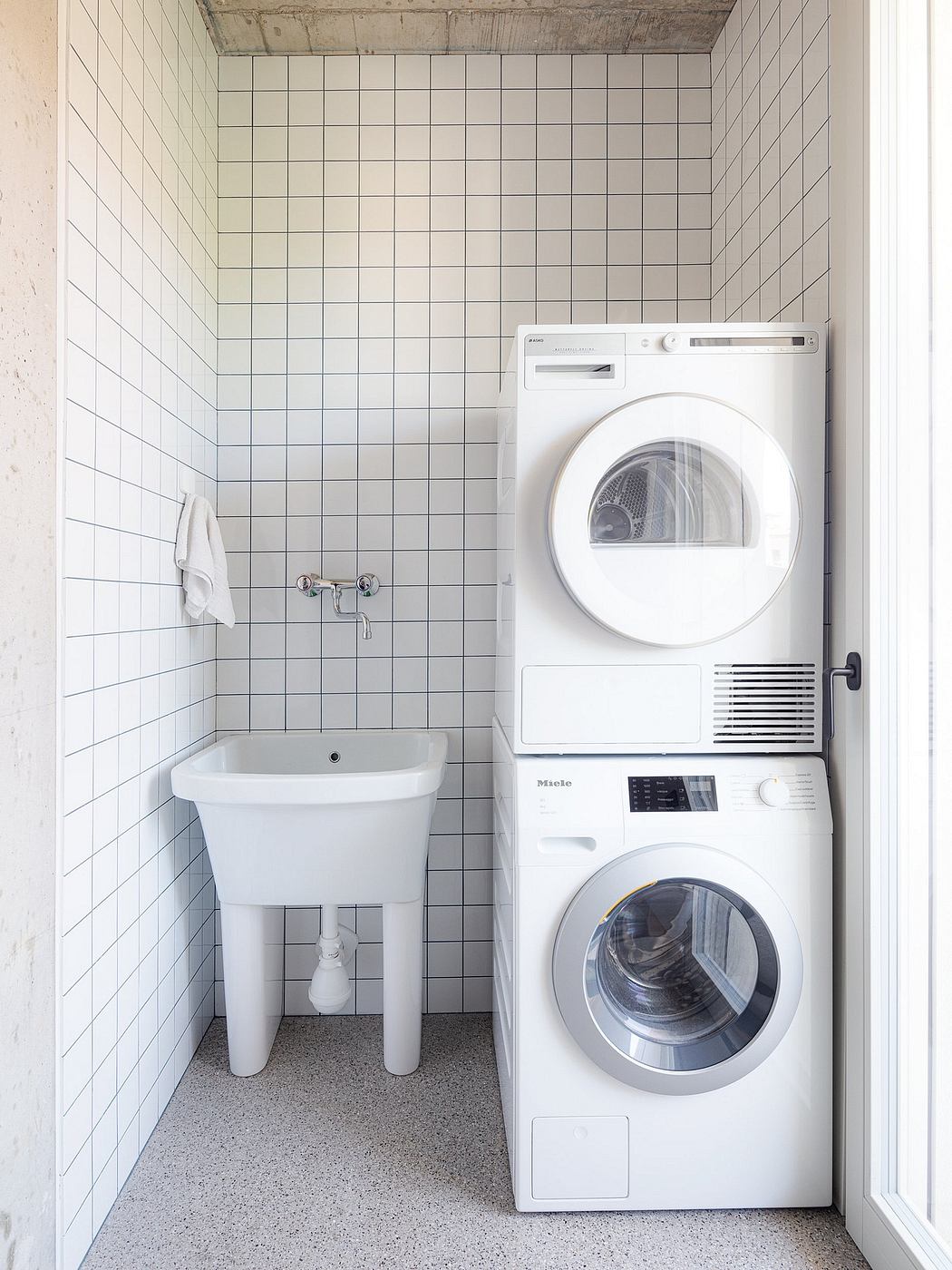 Sleek, minimalist bathroom with white subway tile, Miele washer and dryer, and wall-mounted sink.