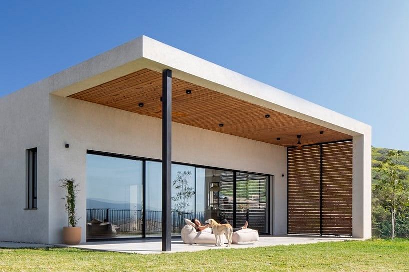 Modern minimalist home with wooden ceiling, large glass windows, and outdoor seating.
