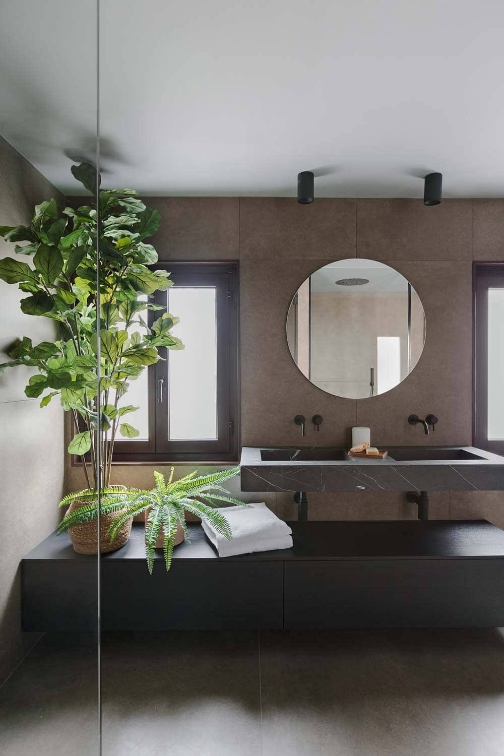 Modern bathroom with sleek black vanity, round mirror, and lush greenery for an inviting look.