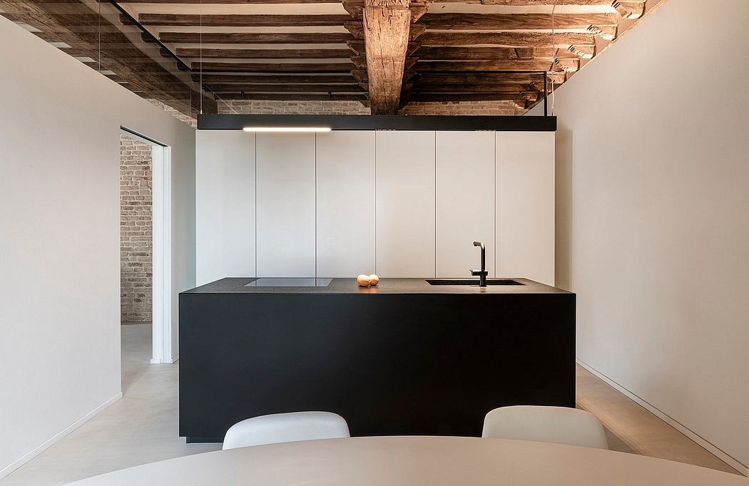 A modern, minimalist kitchen with a sleek black island, wooden beams, and exposed brick walls.