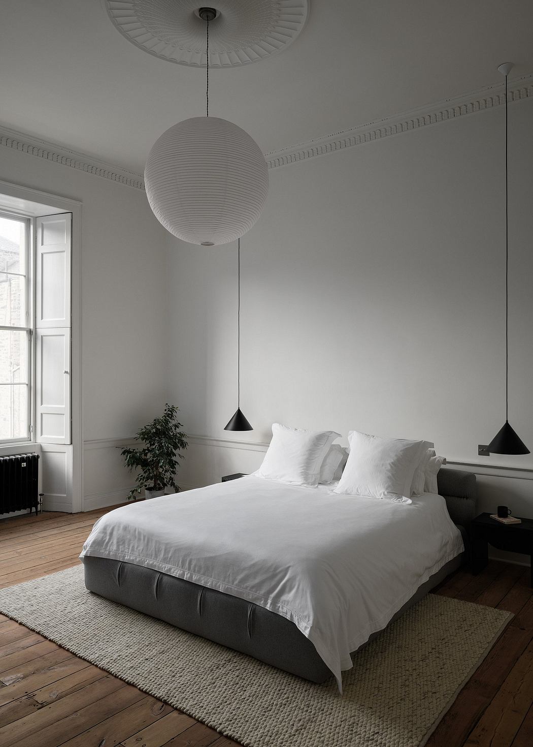 A modern, minimalist bedroom with a large pendant light, wooden floors, and a plush rug.