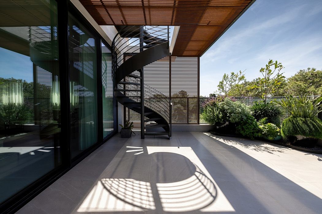 Sleek spiral staircase and glass walls overlooking a lush green garden.