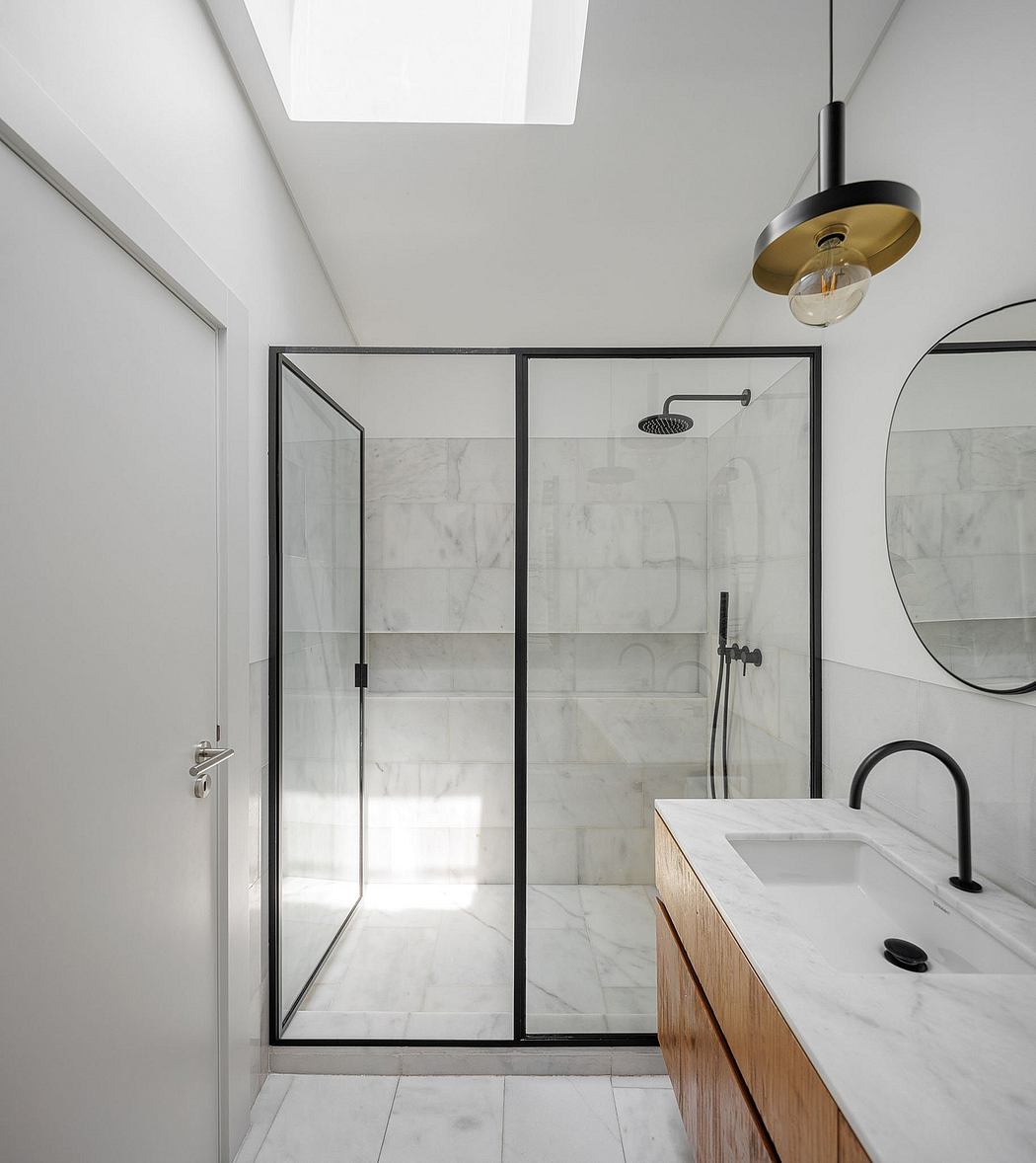 A modern, minimalist bathroom with a marble-tiled shower stall, black framed glass doors, and a wooden vanity.