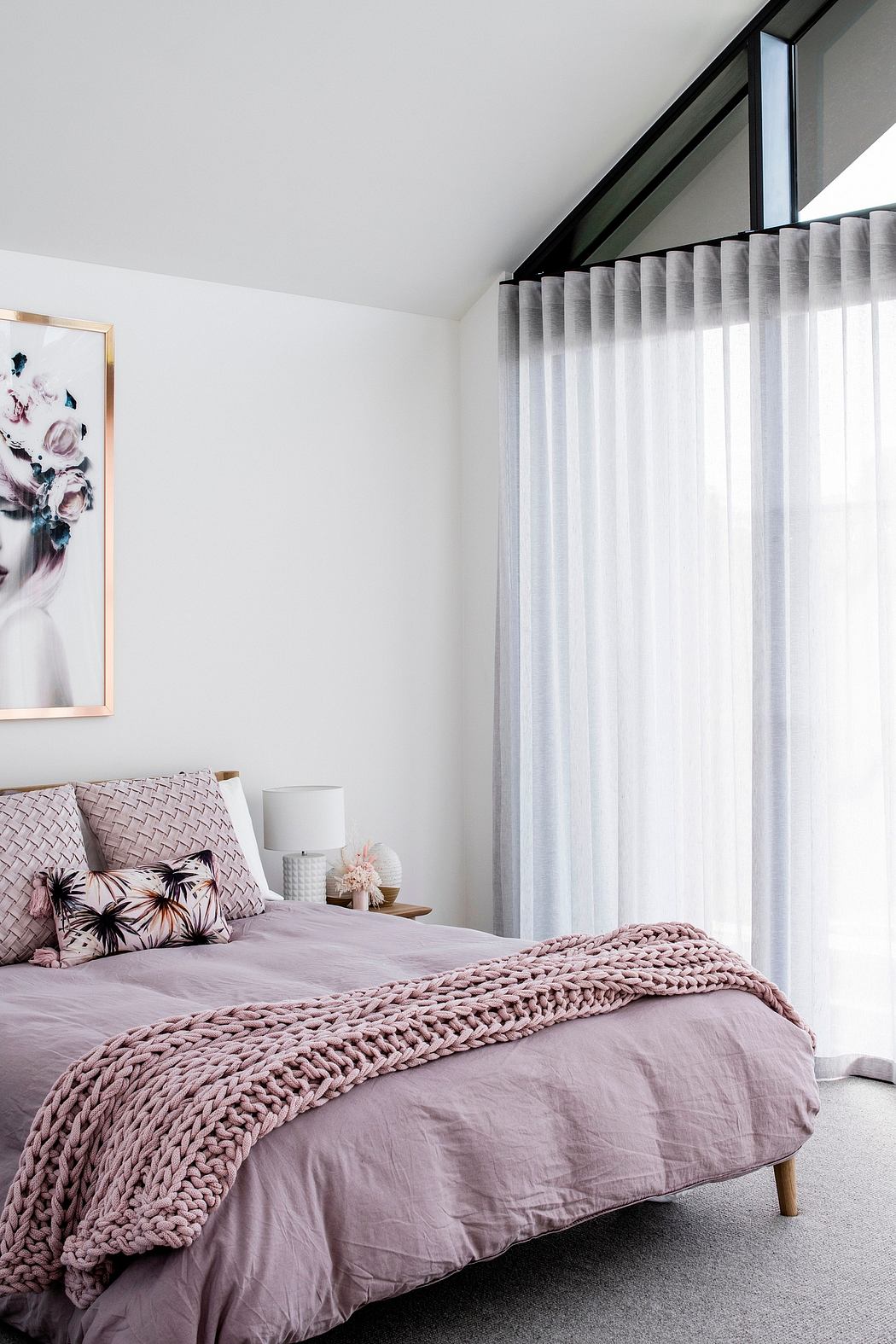 Minimalist bedroom with gray curtains, chunky knit throw, and floral artwork.