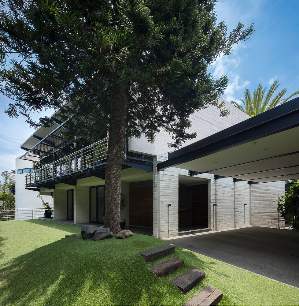 A modern building with a glass facade, overhanging roofs, and a lush green lawn leading to the entrance.