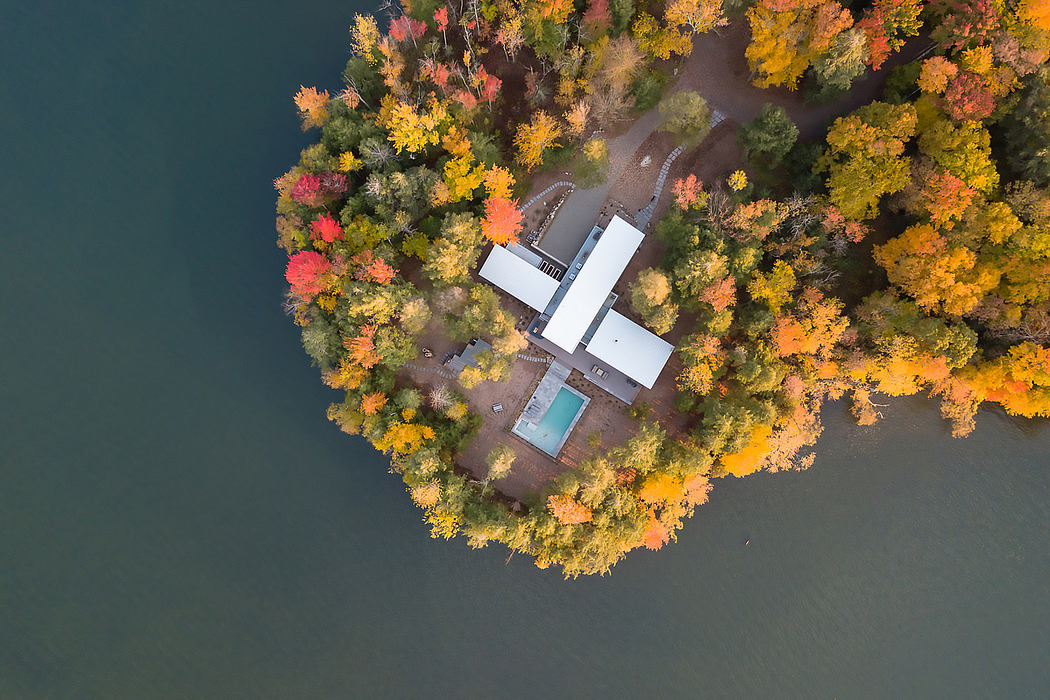 Aerial view of a modern, white-clad building surrounded by vibrant fall foliage.