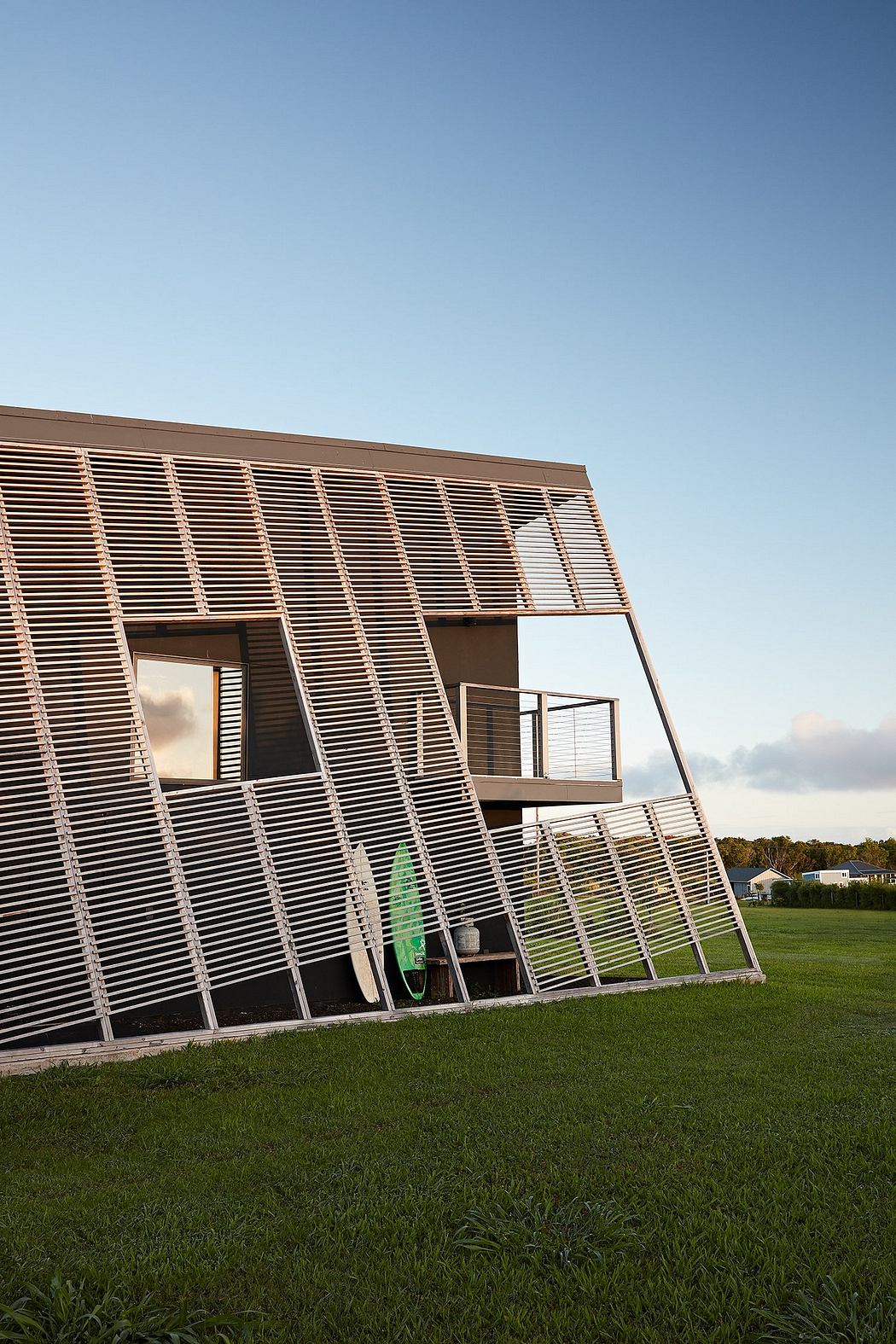 Striking modern architectural facade with intricately patterned wooden slats, balconies, and a verdant grassy foreground.