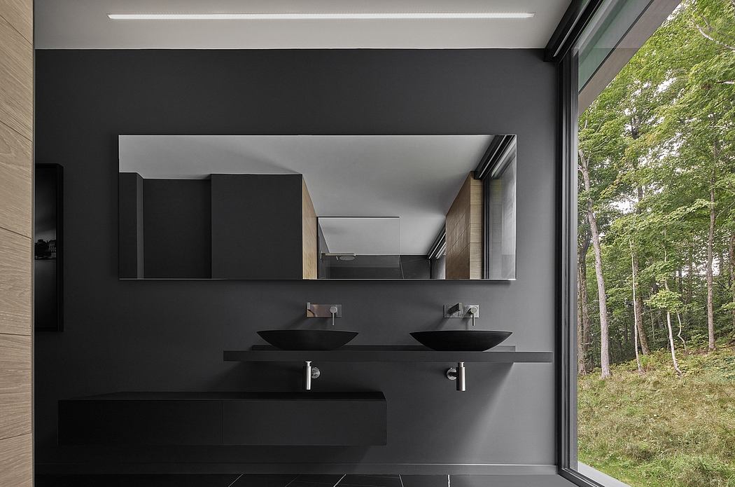 Minimalist bathroom with black vanity and sinks, large window overlooking lush forest.