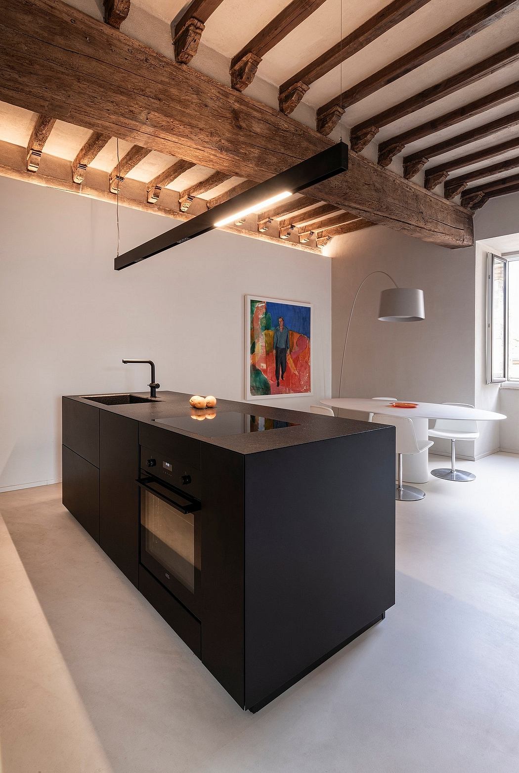 A modern kitchen with rustic wooden beams, a sleek black island, and a colorful painting.
