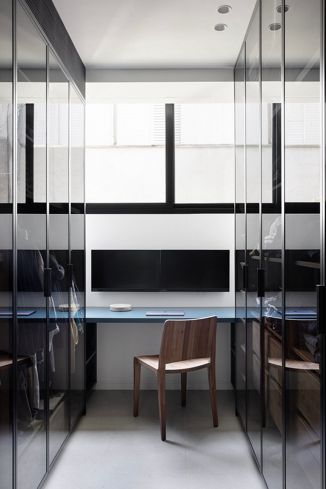 Modern minimalist interior with sleek glass panels, wooden chair, and built-in storage.