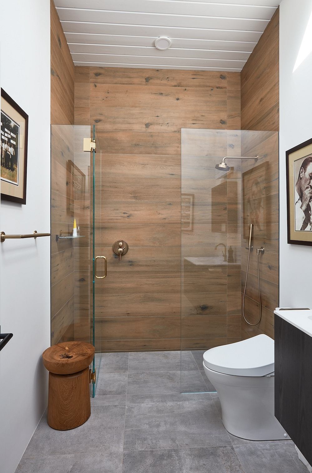 Modern bathroom with rustic wood paneling, glass shower, and concrete floor tiles.