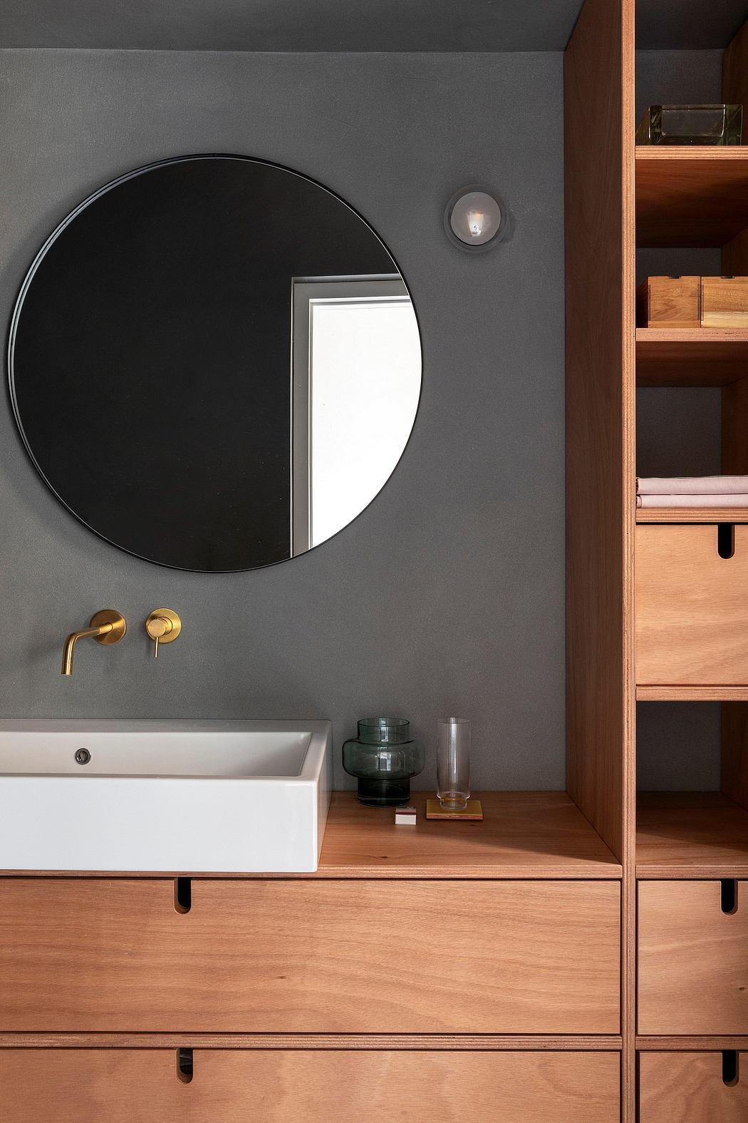 Minimalist bathroom with a large round black mirror, wood vanity, and built-in shelving.