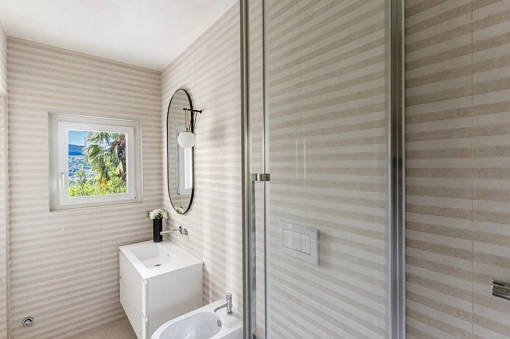 Sleek, modern bathroom with striped wallpaper, round mirror, and glass shower enclosure.