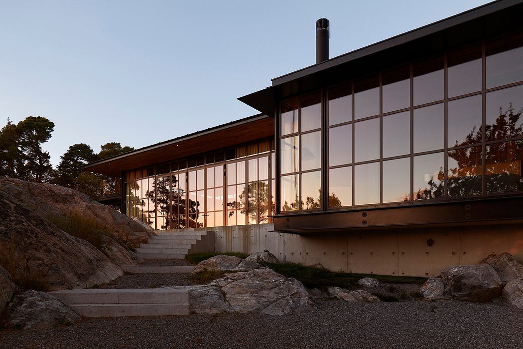 A modern glass and wood structure with a sloping roof and steps leading up to it, reflecting the sunset.