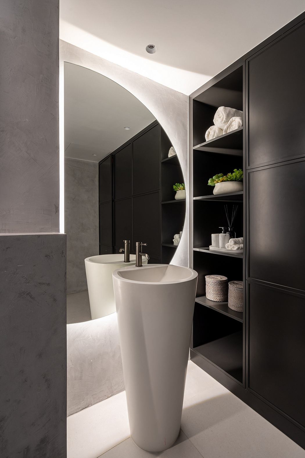 A modern bathroom with a freestanding white pedestal sink, black cabinetry, and shelving.