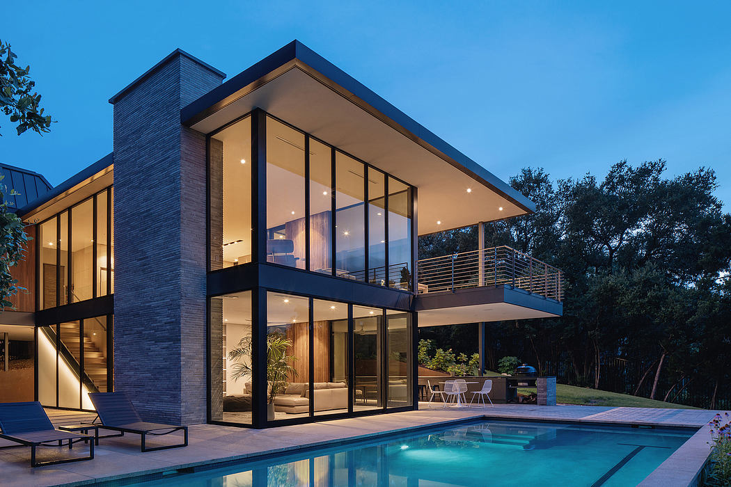 Modern two-story home with expansive glass walls, covered patio, and pool surrounded by trees.