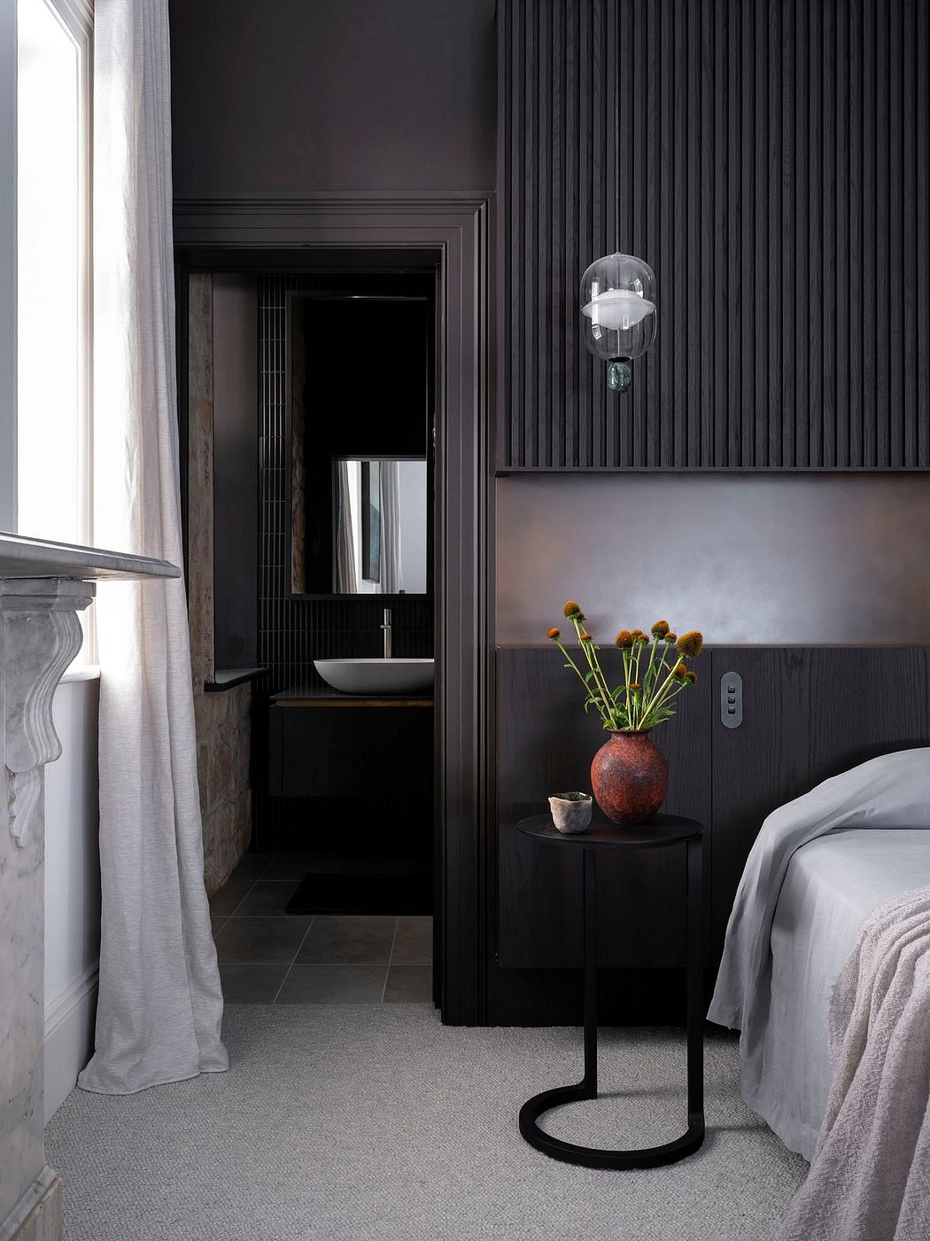 Dark, moody bedroom with minimalist decor, sleek vanity, and decorative vase with flowers.