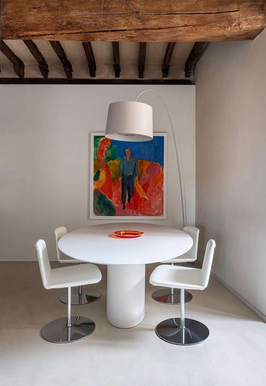 A modern dining space featuring a white table, chrome chairs, and a colorful painting.
