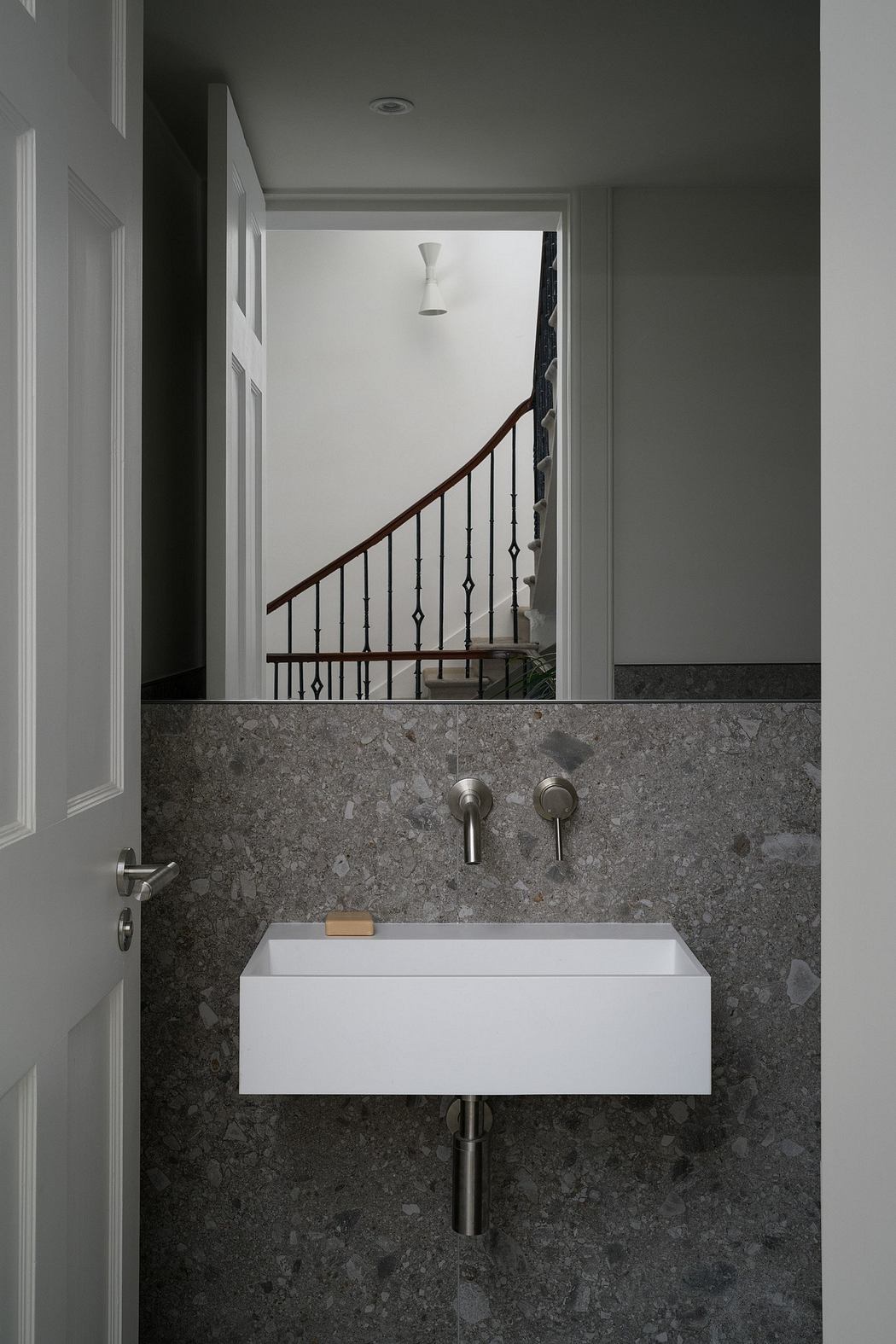 A modern bathroom with a white sink basin, wooden staircase railing, and gray marble walls.