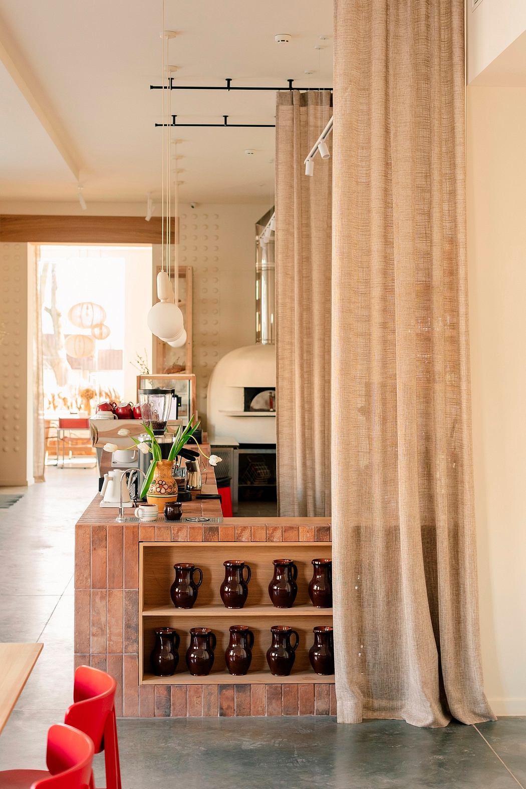 A cozy interior with curtains, a tiled storage unit displaying ornate pitchers, and warm lighting.