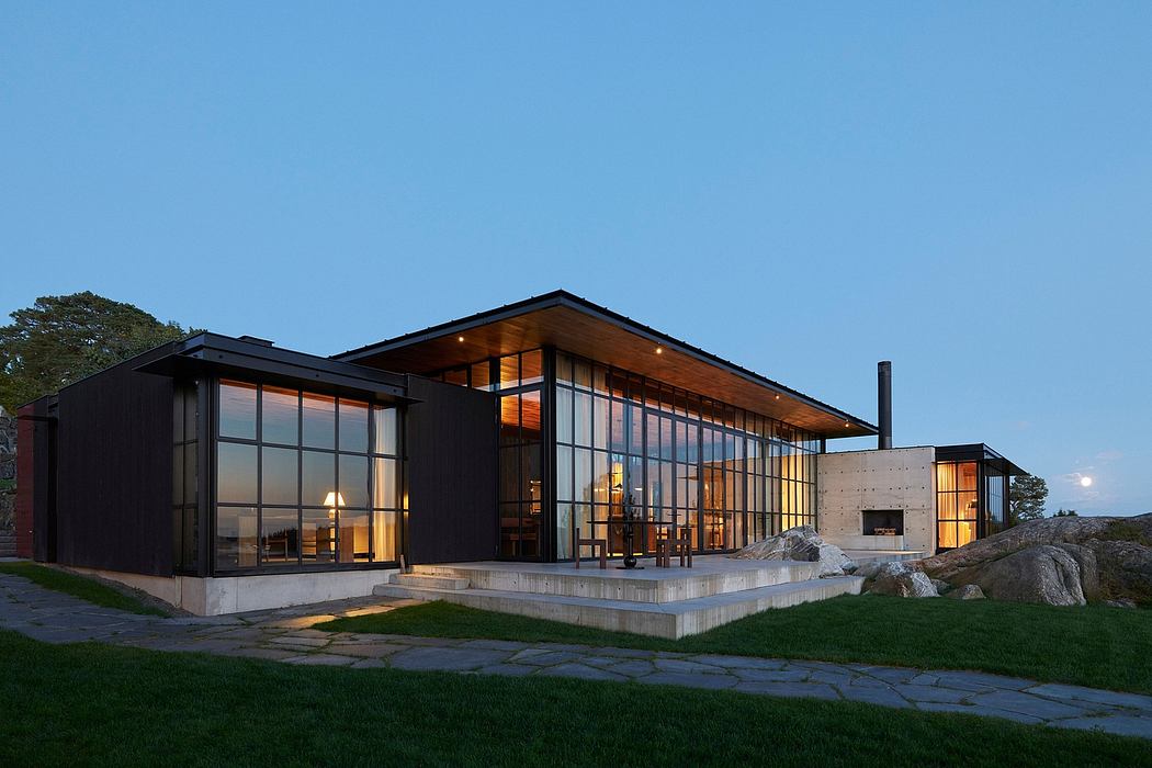 A modern, glass-walled house with a wooden roof and outdoor patio, set against a scenic backdrop.