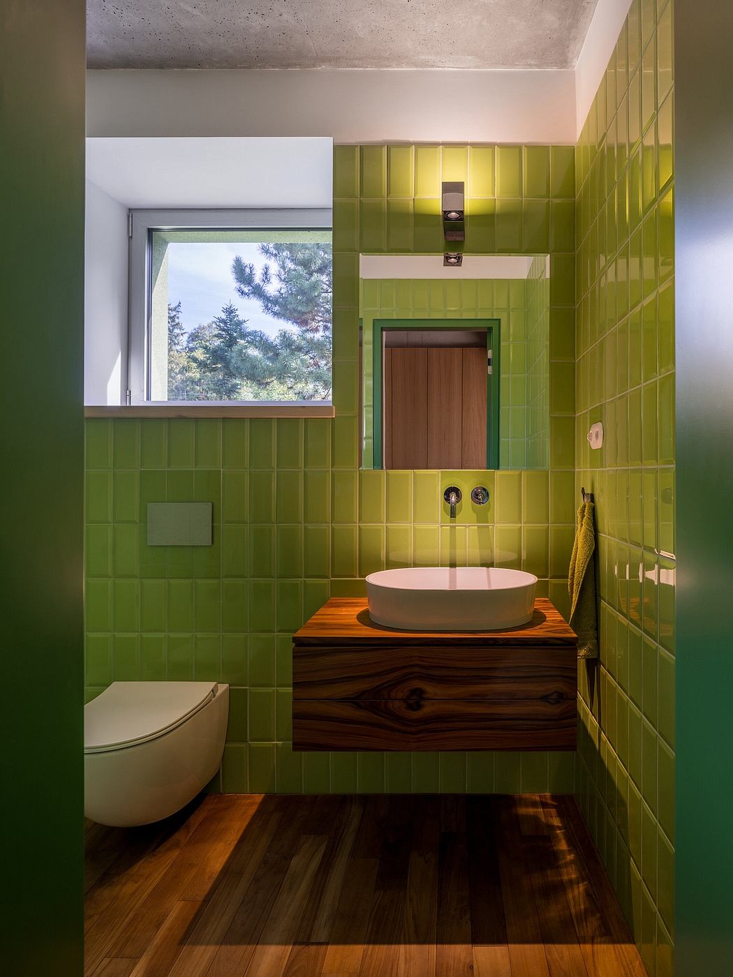 Vibrant green tile, rustic wood vanity, and a window with a forest view create a striking bathroom design.