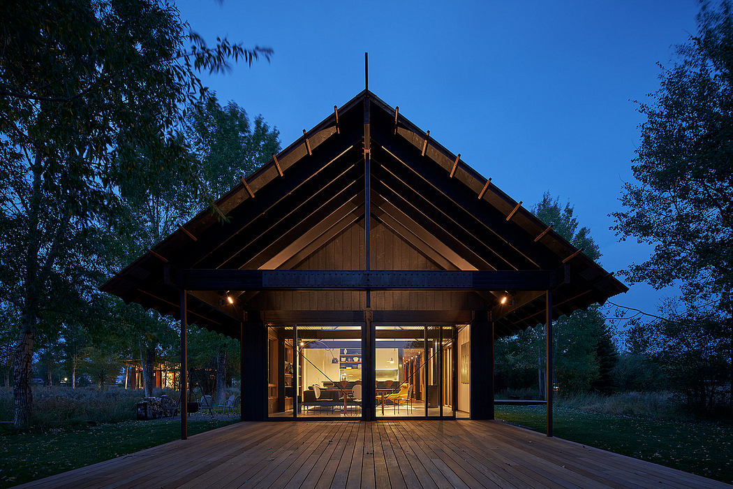 A rustic wooden lodge with a sloped roof and a large covered porch overlooking a serene landscape.