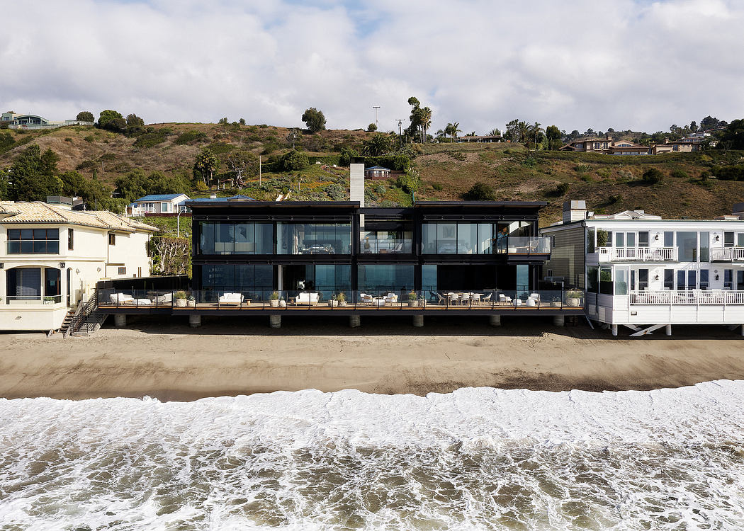 Modern glass and steel beachfront home with expansive patio and ocean views.