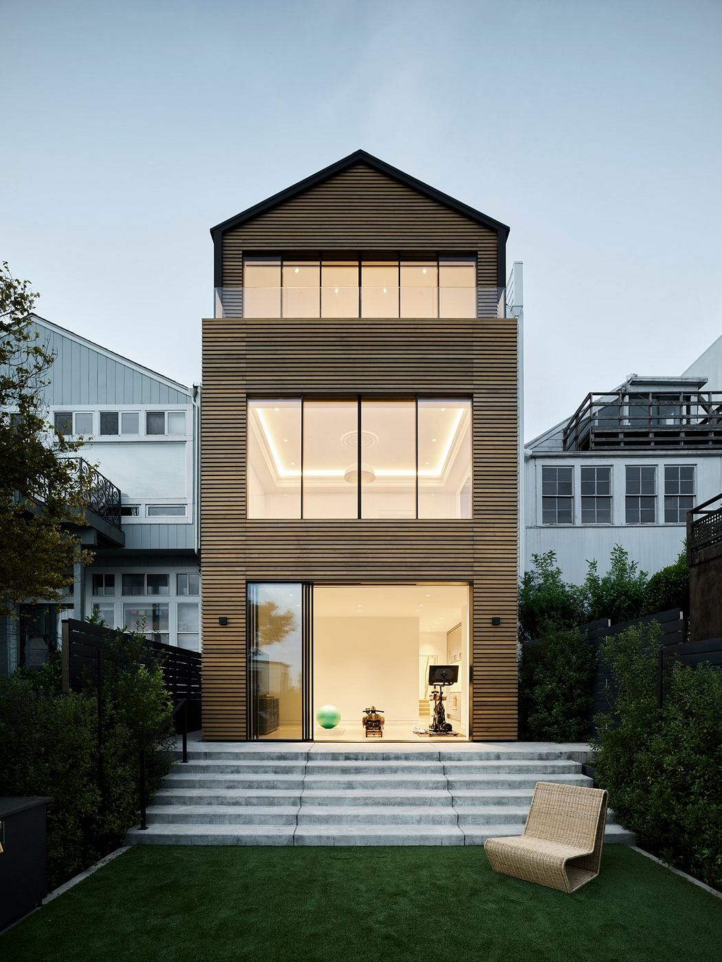 A modern, two-story home with a striking black and wood exterior, large windows, and a lush lawn.